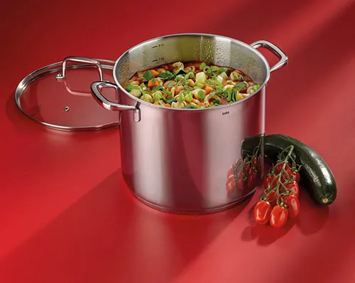 Suppentopf Edelstahl mit Gemüsesuppe und frischem Gemüse Großer Edelstahl-Suppentopf mit Glasdeckel gefüllt mit Gemüsesuppe, daneben frische Tomaten, Gurke und Paprika auf rotem Hintergrund.