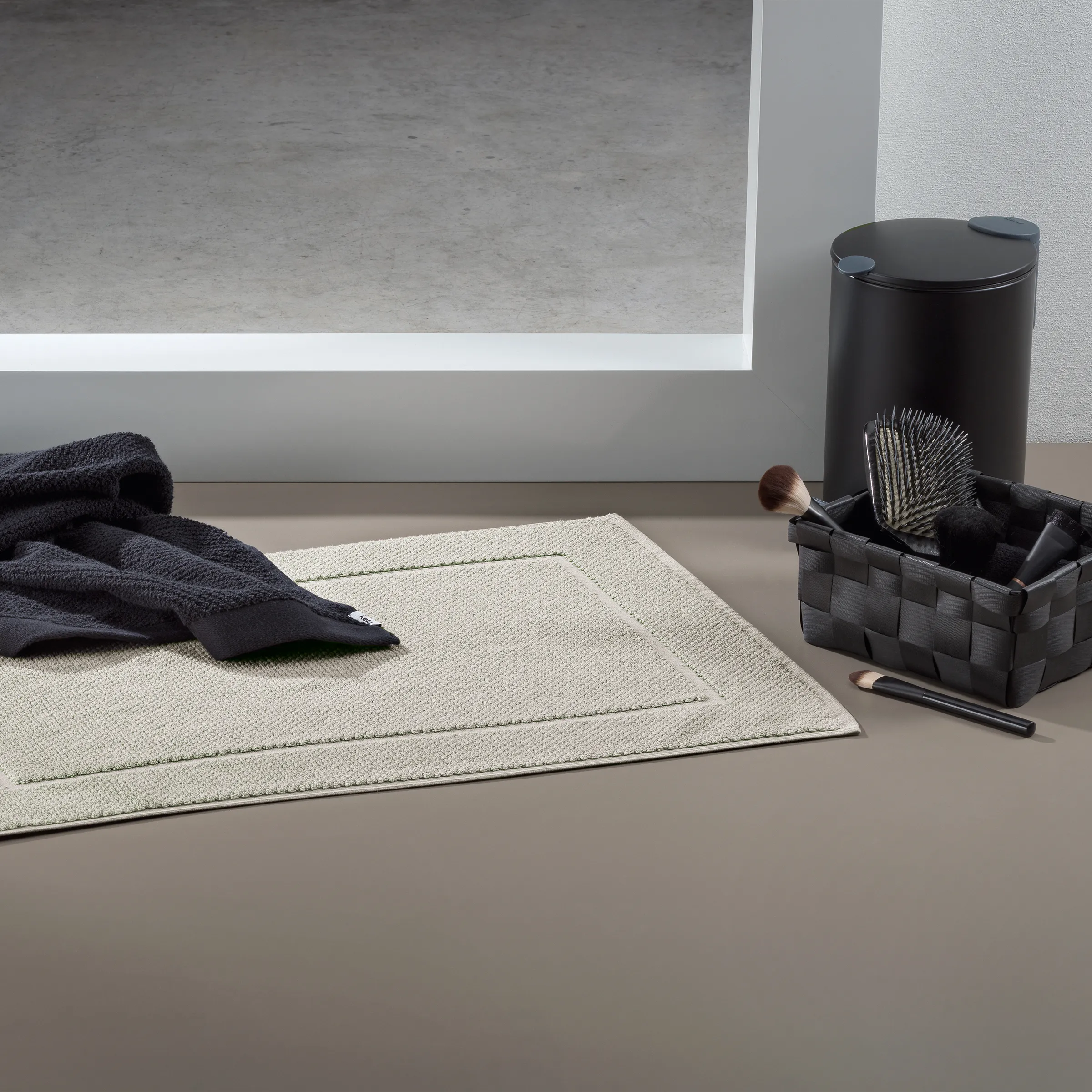 Badezimmer Accessoires Set mit Badematte und Organizer Badezimmer-Arrangement mit beigem Badematte, schwarzem Handtuch, schwarzem Behälter mit Bürste und Kosmetikprodukten