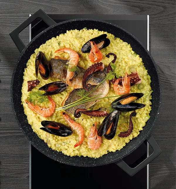 Spanische Paella Meeresfrüchte Rezept Paella in schwarzer Pfanne mit Meeresfrüchten, Garnelen, Muscheln und Fisch auf Holztisch