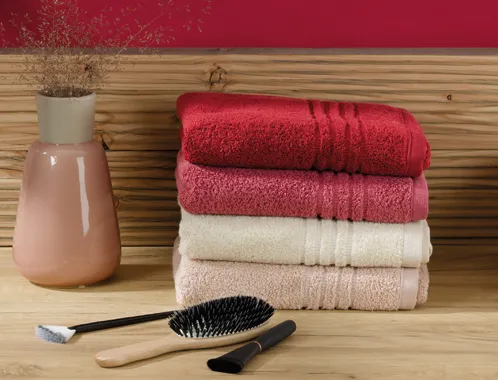 Premium Handtücher Set - Baumwolle in Rot, Creme und Beige Stapel farbiger Handtücher neben Zahnbürsten und Vase auf Holzoberfläche