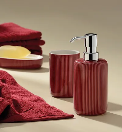 Badezimmer-Set mit bordeaux-roten gerippten Behältern, Seifenspender mit Chromaufsatz, gelber Seife und roten Handtüchern