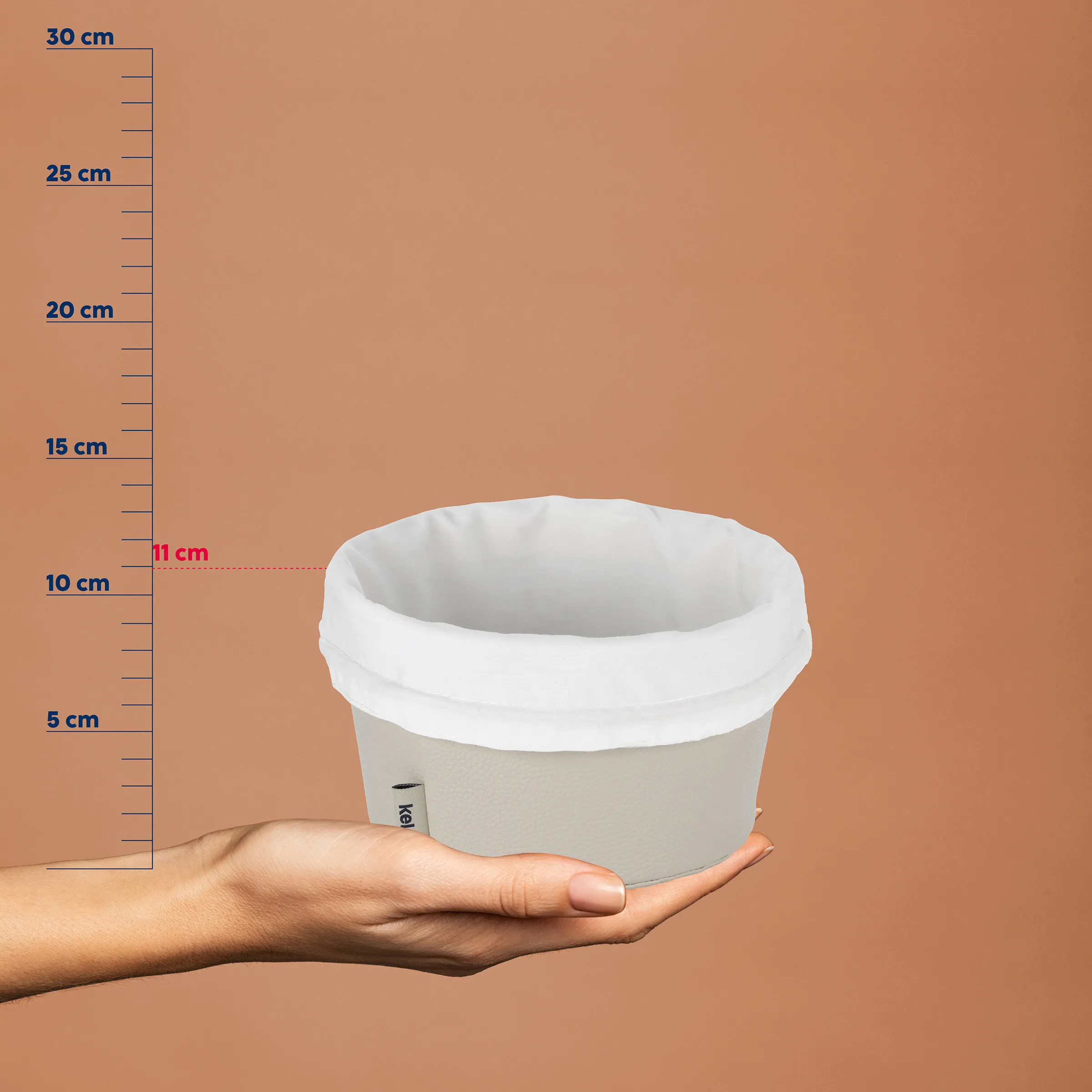 Hand hält grauen Stoffkorb mit weißem Rand vor Maßstab, Höhe 11 cm