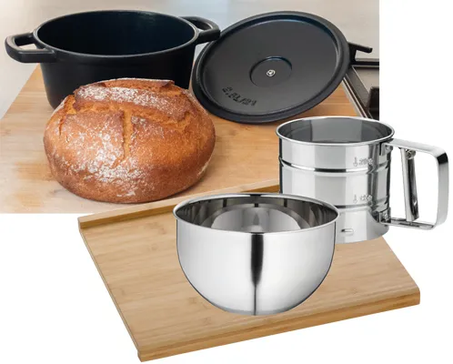 Küchenset mit schwarzem Bräter, frischem Brot auf Holzbrett und silbernen Edelstahlbehältern