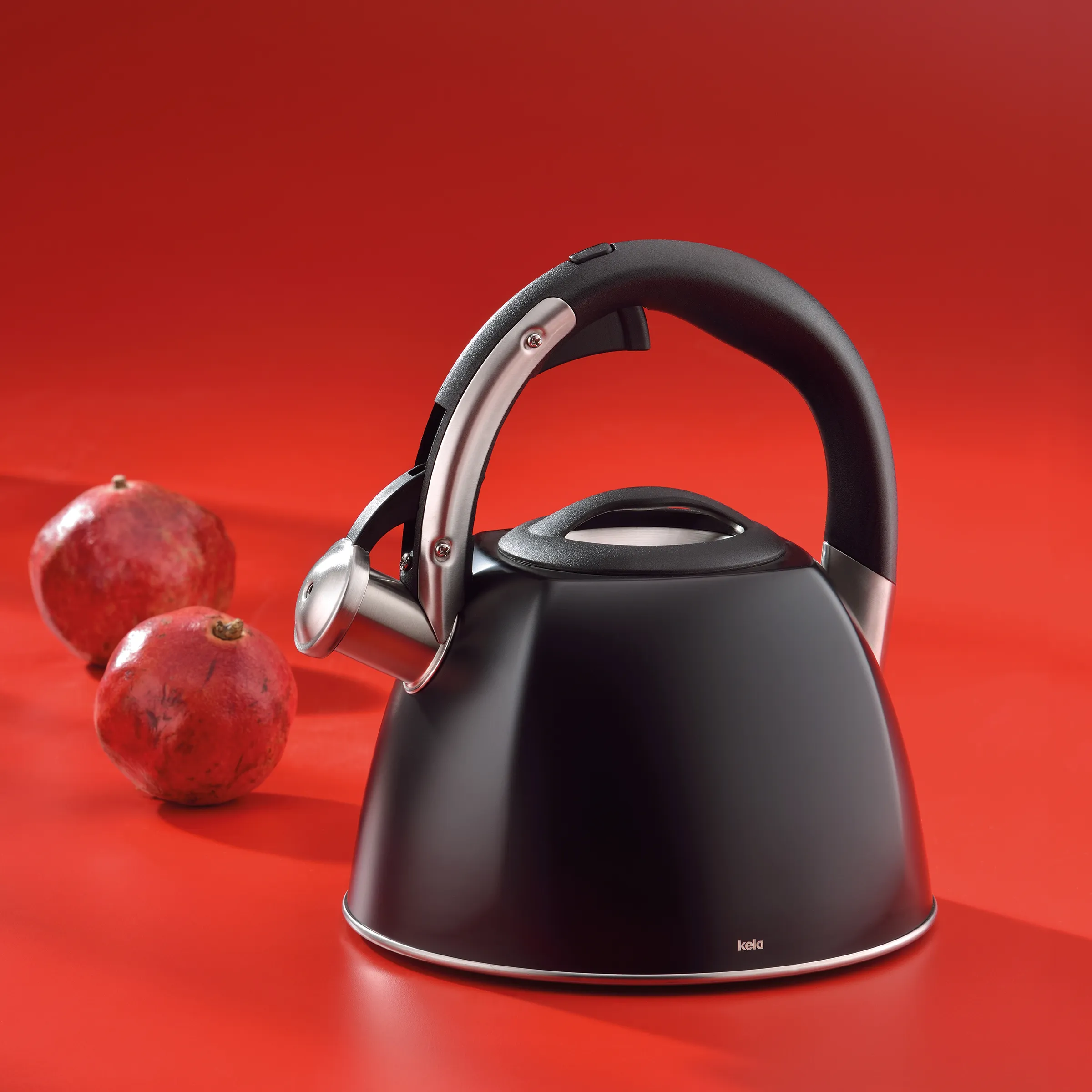 Flötenkessel schwarz mit Edelstahl-Griff – Wasserkessel Kela für die moderne Küche Schwarzer Flötenkessel mit roségoldenem Griff auf rotem Hintergrund, dekoriert mit drei roten Äpfeln