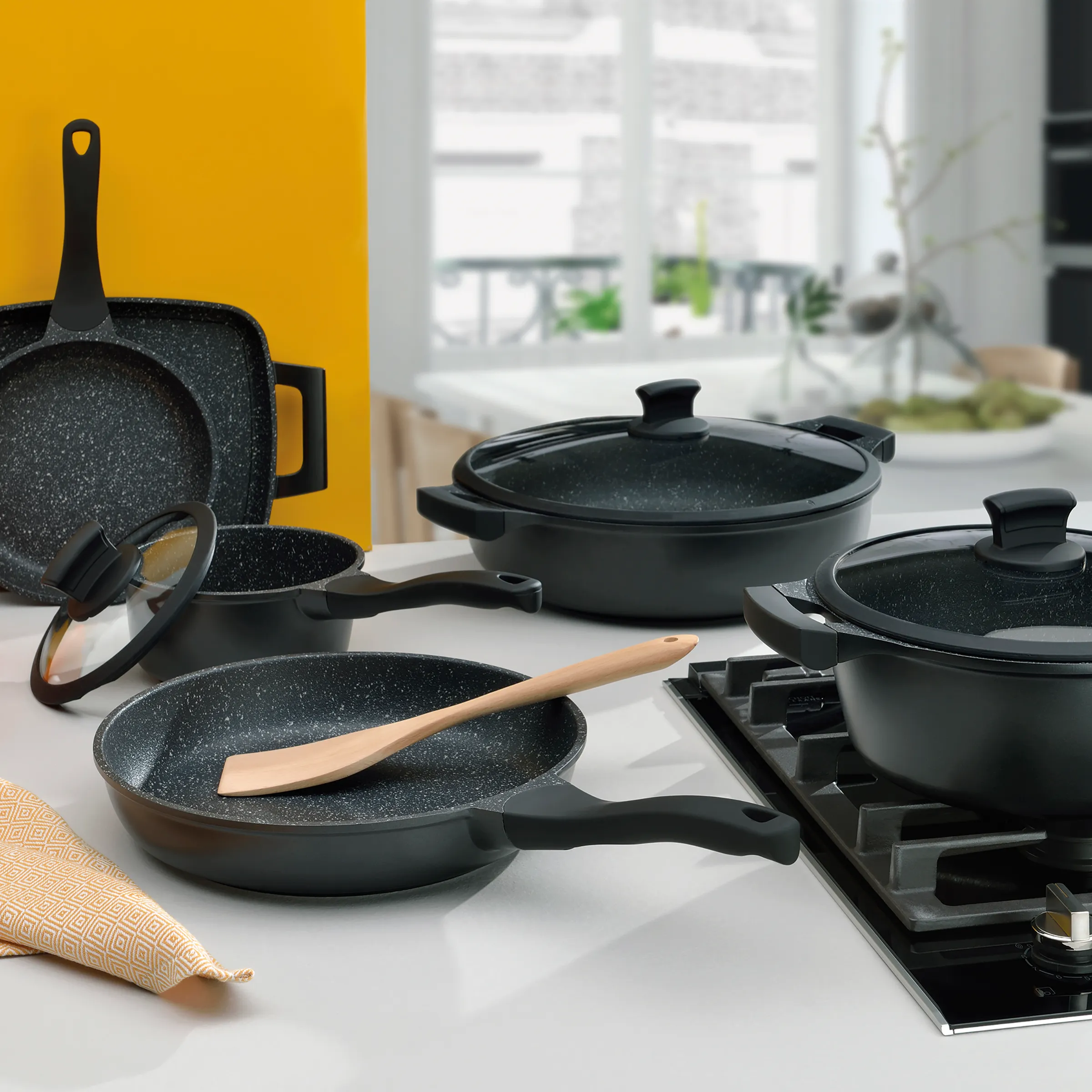 Antihaft-Kochgeschirr-Set schwarz - Pfannen und Töpfe mit Marmorbeschichtung Schwarze Antihaft-Kochgeschirr-Set mit Pfannen, Töpfen und Holzspatel auf weißer Küchenarbeitsplatte