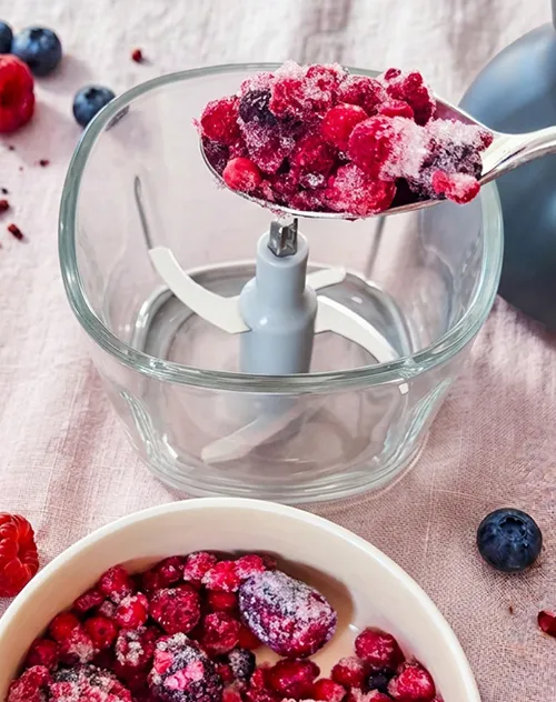 Food Processor Beeren schneiden - Küchenmaschine Küchenmaschine mit Aufsatz füllt Schaufel mit roten und schwarzen Früchten, daneben Schale mit Beeren