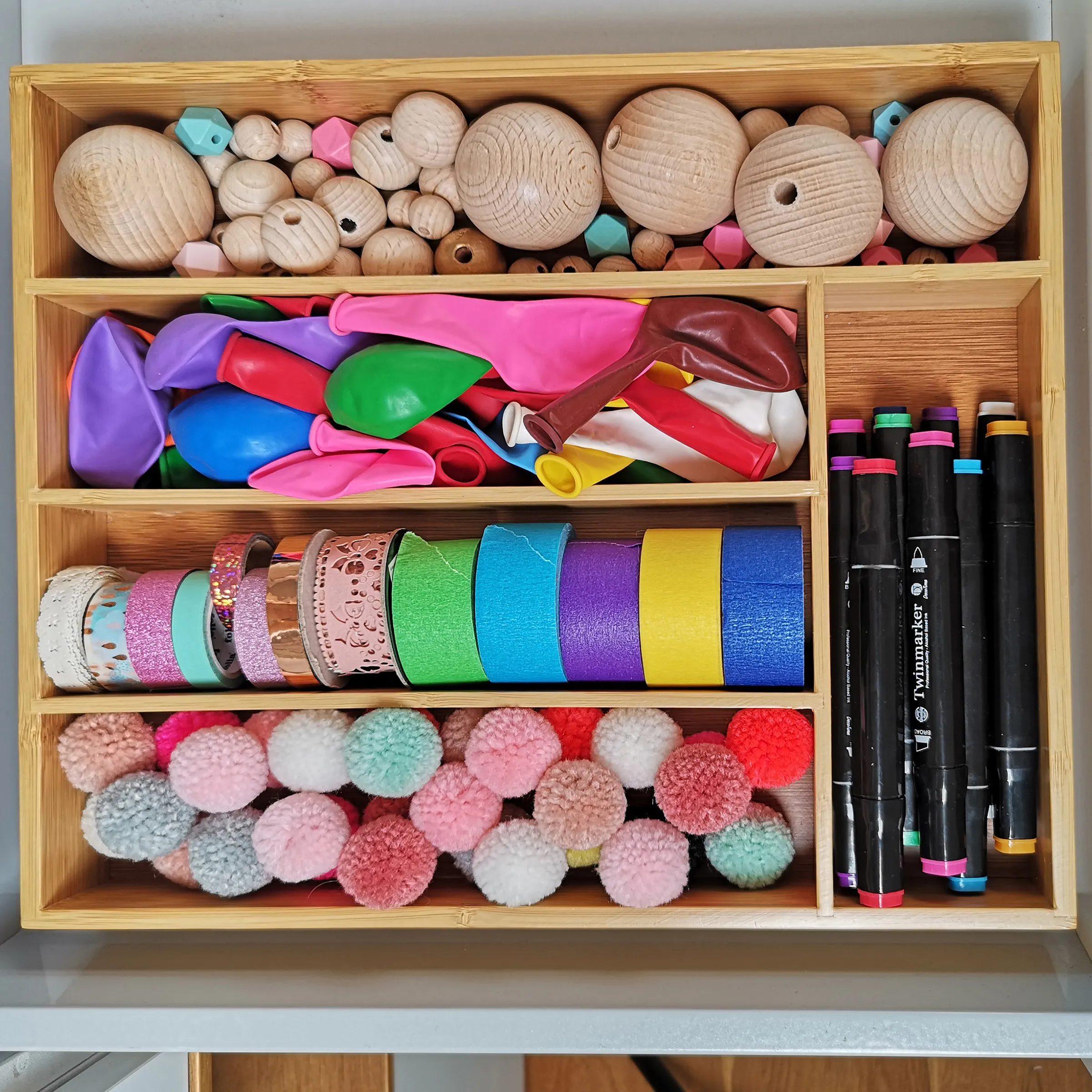 Bastelbox Organizer mit Holzperlen, Bändern und Pompons Holzkasten mit organisierten Bastelmaterialien: Holzperlen, bunte Bänder, Pompons, Marker und Deko-Elementen in verschiedenen Farben.