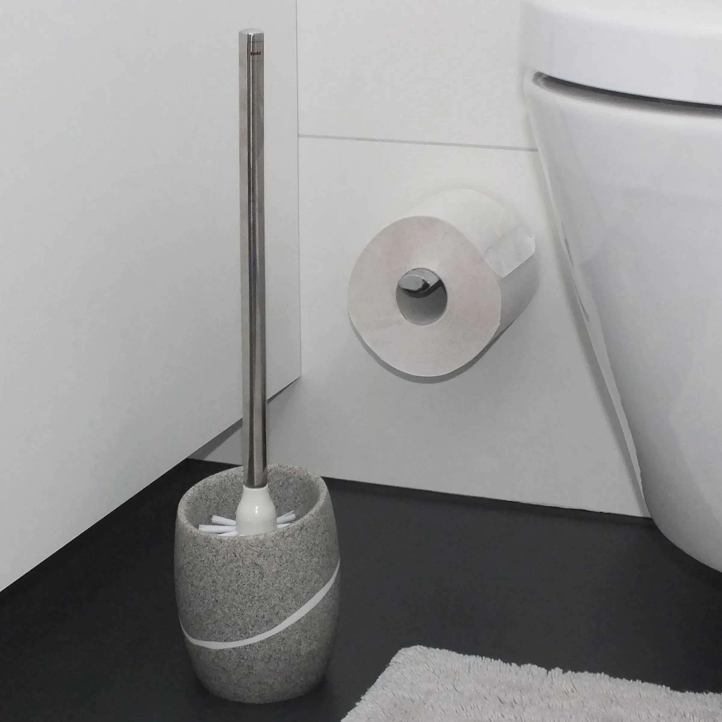 Toilettenbürste mit Steinhalter und WC-Zubehör - Badezimmer Design Moderne Toilettenbürste mit grauem Steinhalter neben Klorollenhalter und weißem WC in minimalistischem Bad