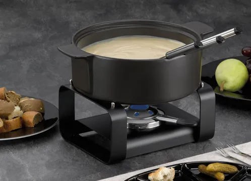 Fondue Set Käse schwarz elektrisch Brenner Schwarzes Fondue-Set mit Käsecreme in schwarzem Topf, Brenner, Gabel und Gemüse-Beilagen auf grauem Untergrund
