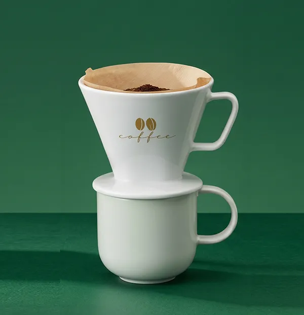Kaffeefilter Set Porzellan - Handfilter mit Tasse für Pour Over Kaffee Weißer Keramik-Kaffeefilter mit Goldaufdruck auf passender Tasse vor grünem Hintergrund