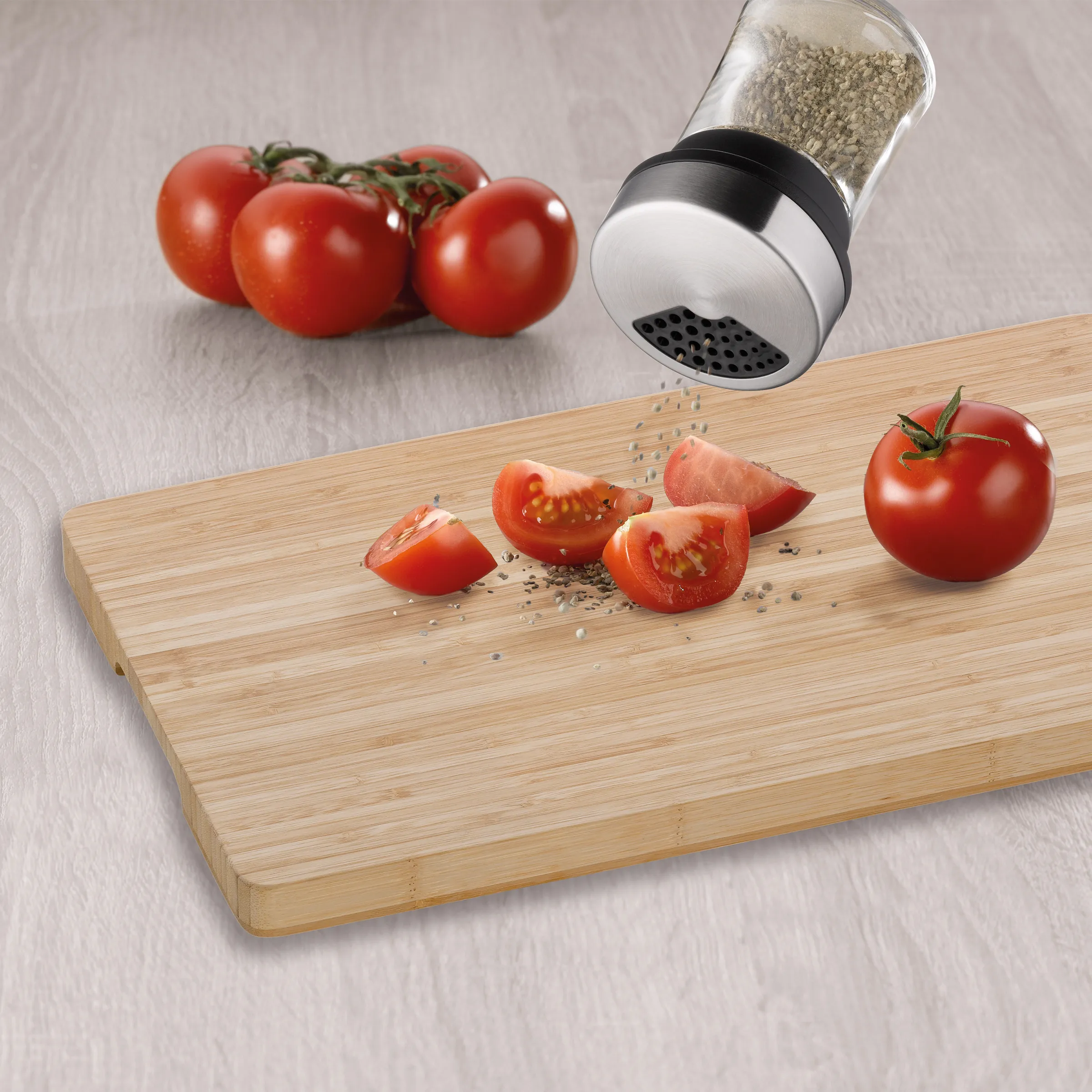 Holzschneidebrett mit halbierten Tomaten und Salzstreuer, der Salz über das Gemüse verteilt