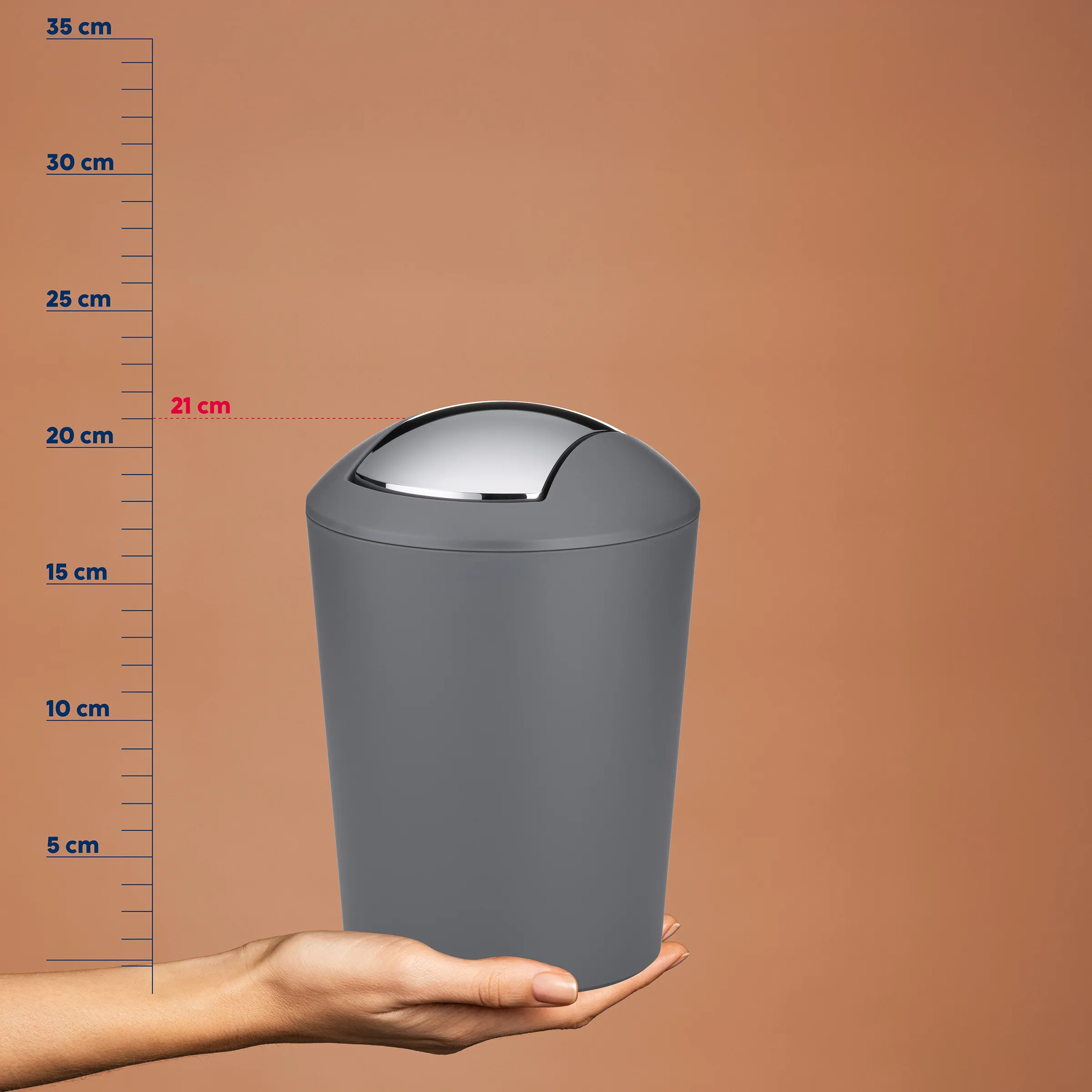 Schwingdeckel-Abfalleimer grau 21 cm - kompakter Kosmetikeimer für Bad Grauer Schwingdeckel-Abfalleimer wird auf einer Hand präsentiert mit Größenskala von 21 cm Höhe