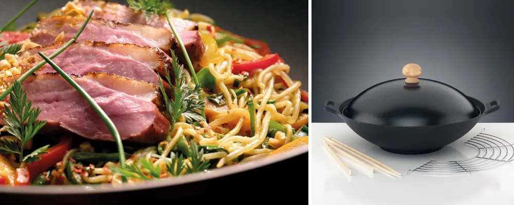 Gebratene Entenbrust mit Asia-Nudeln und Wok-Set für asiatische Küche Gebratene Entenbrustringe mit Nudeln, Gemüse und Kräutern auf Teller, daneben schwarzer Wok mit Holzdeckel