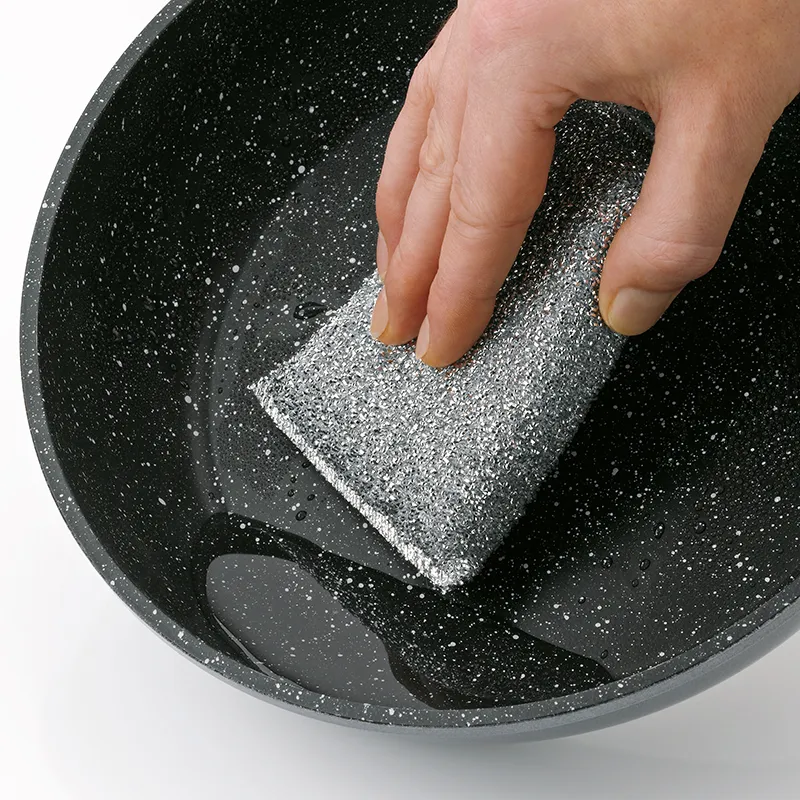 Steel wool scrubbing sponge for pans and cookware Hand cleaning black pan with steel wool sponge against white background