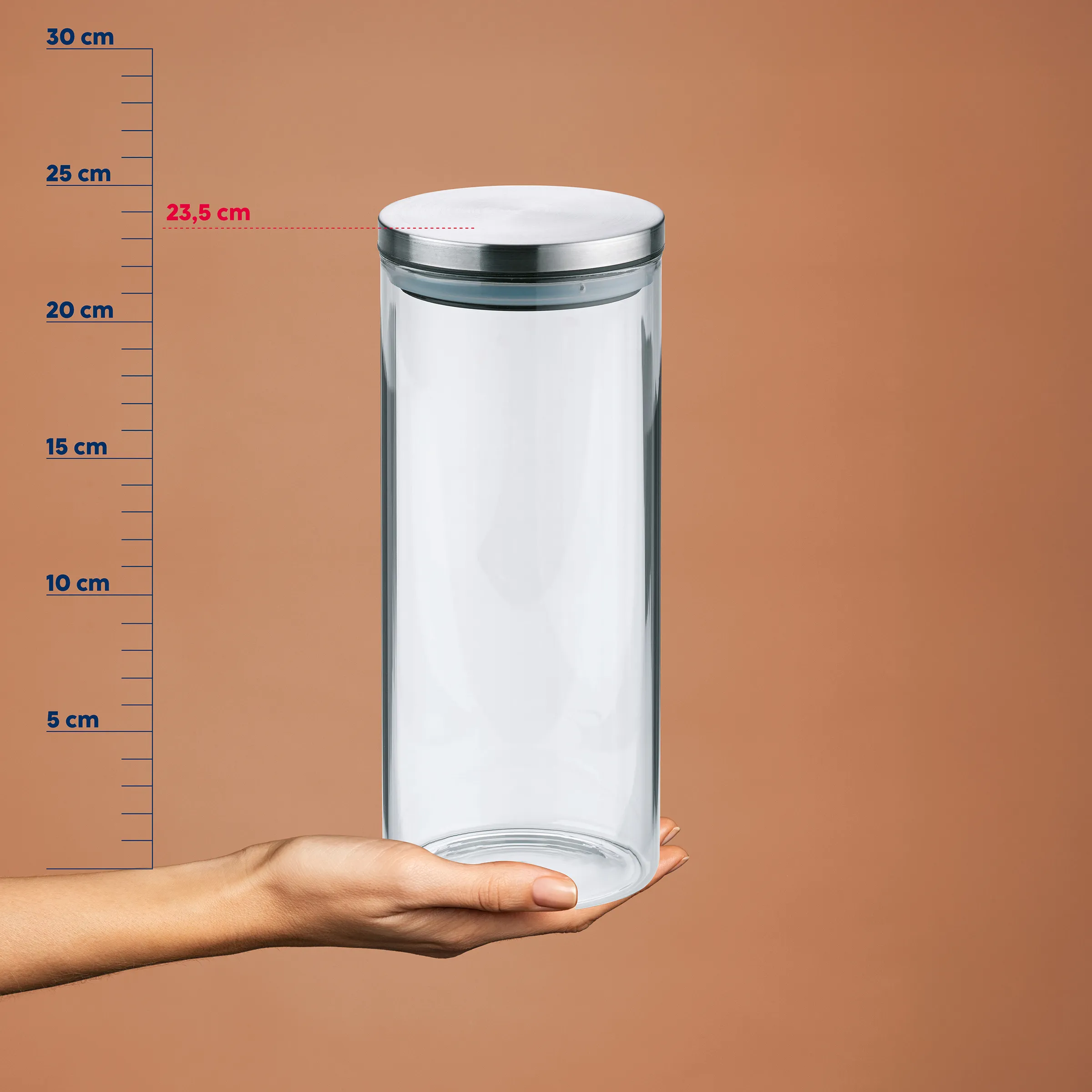 Cylindre en verre avec couvercle en métal sur une paume devant une échelle de mesure, diamètre 23,5 cm, hauteur environ 25 cm