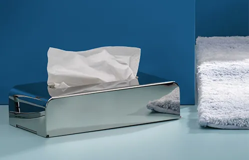 Taschentuchspender Chrom Design - moderner Kosmetiktuchbox für Badezimmer Verchromter Taschentuchspender mit weißen Tüchern auf blauem Hintergrund neben weißen Handtüchern