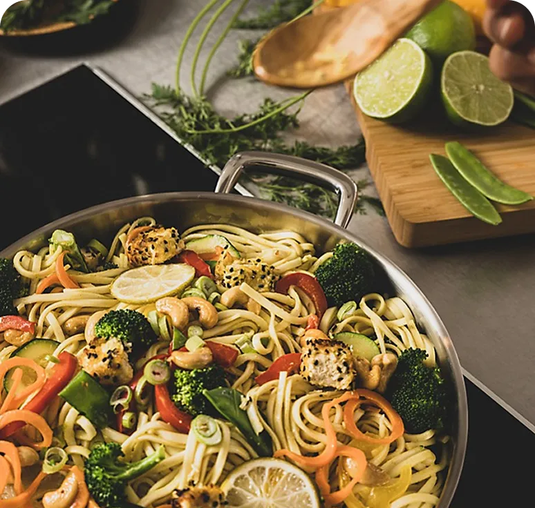 Asian Noodle Stir-Fry with Shrimp and Vegetables Asian noodle stir-fry with vegetables, shrimp and cashews in large wok, lime and fresh herbs on the side