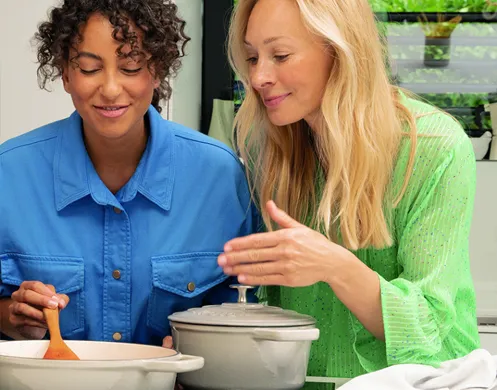 Frauen kochen zusammen - Küchen Teamwork und Rezepte Zwei Frauen kochen zusammen in einer Küche. Die eine trägt ein blaues Hemd, die andere ein grünes Strickoberteil.