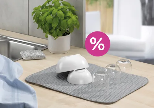 Küchengeschirr Abfluss Abtropfmatte mit Rabatt Küchencounter mit weißem Küchengeschirr auf grauer Matte, Topfpflanze und rosa Rabatt-Sticker