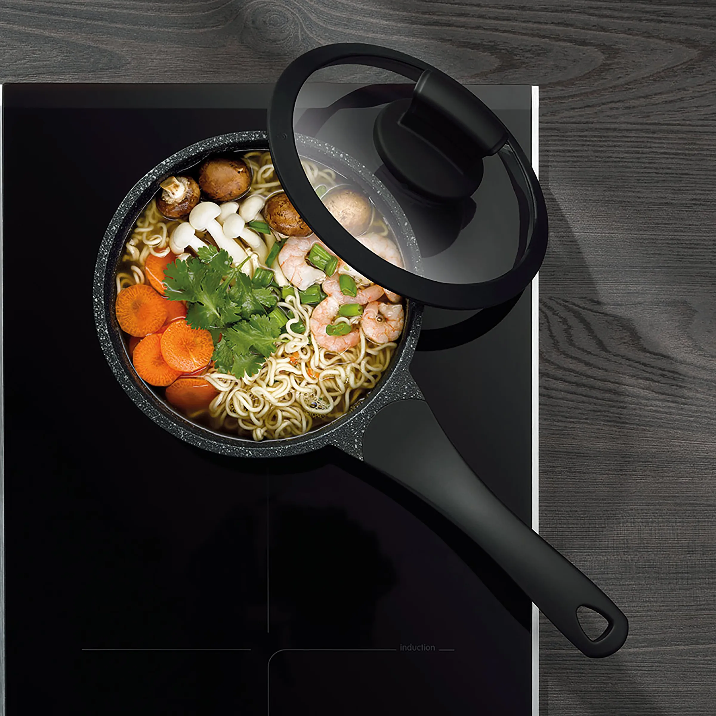 Induktions-Kochtopf mit Nudelsuppe - hochwertiges Kochgeschirr Schwarzer Kochtopf mit Deckel auf Induktionsherd, gefüllt mit Nudelsuppe mit Gemüse, Shrimps und Pilzen