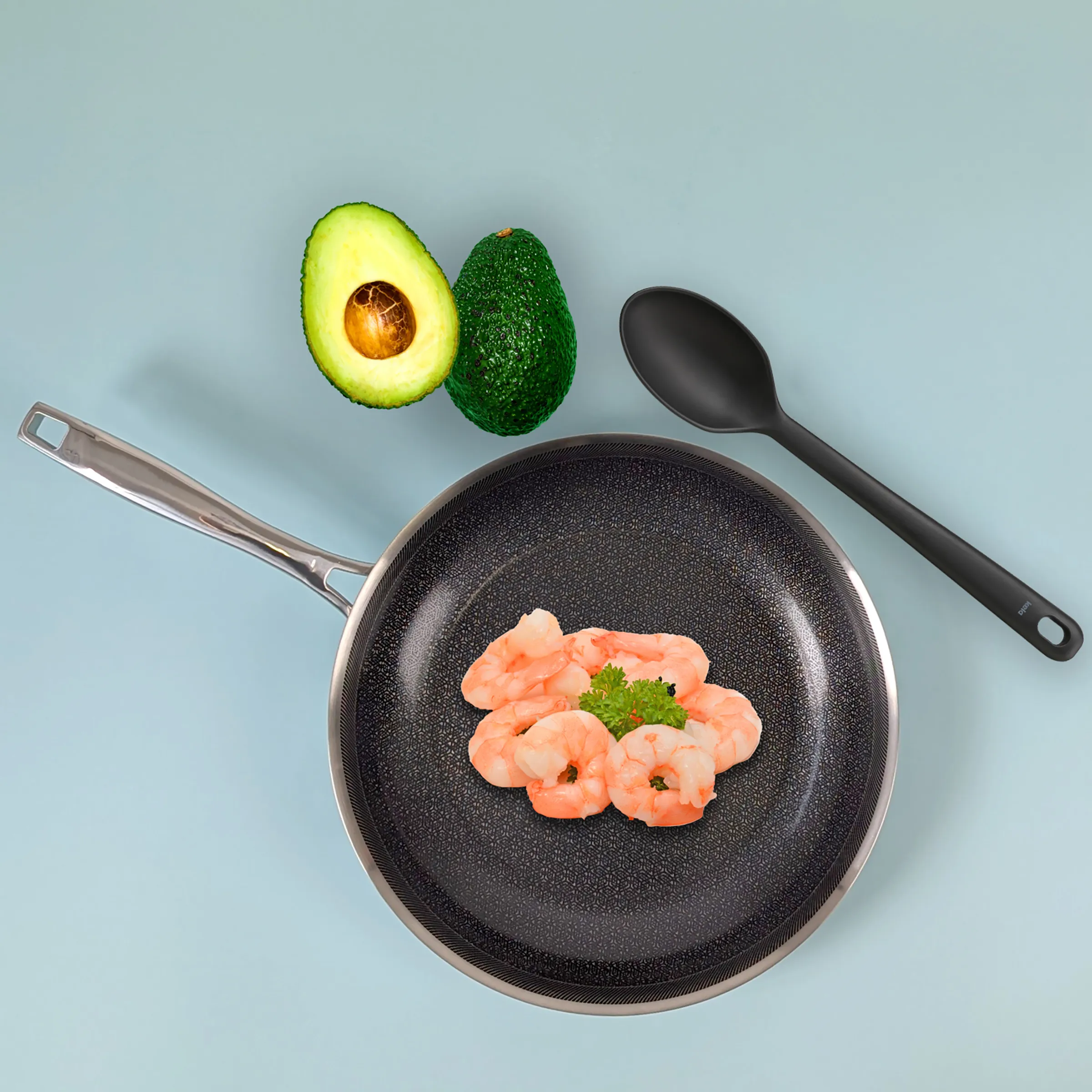 Garnelen Pfanne braten - Antihaft-Kochgeschirr mit Avocado Schwarze Antihaft-Pfanne mit gebratenen Garnelen und Petersilie, daneben halbierte Avocado und schwarzer Kochlöffel auf blauem Hintergrund