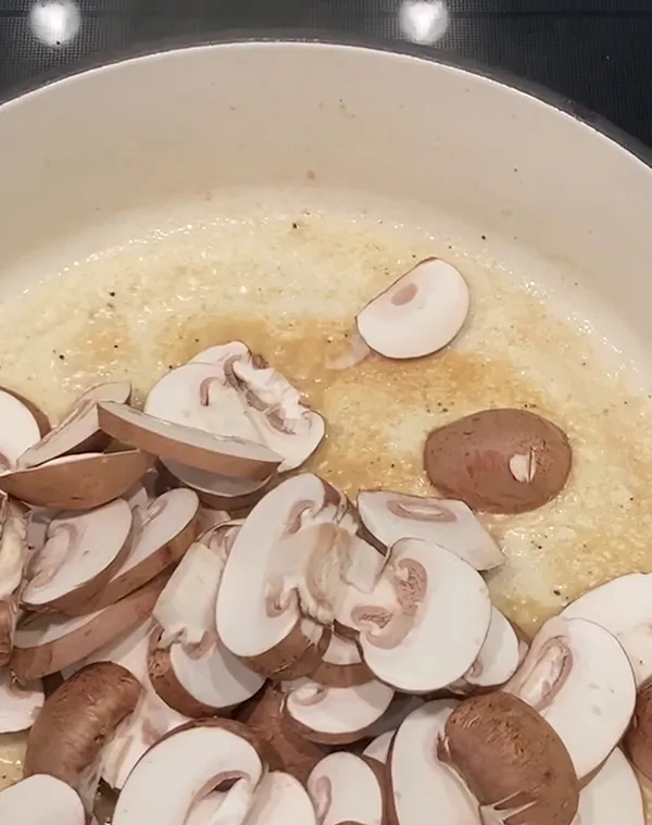 Geschnittene Pilze und Zwiebeln in cremiger Soße in einer weißen Pfanne beim Kochen