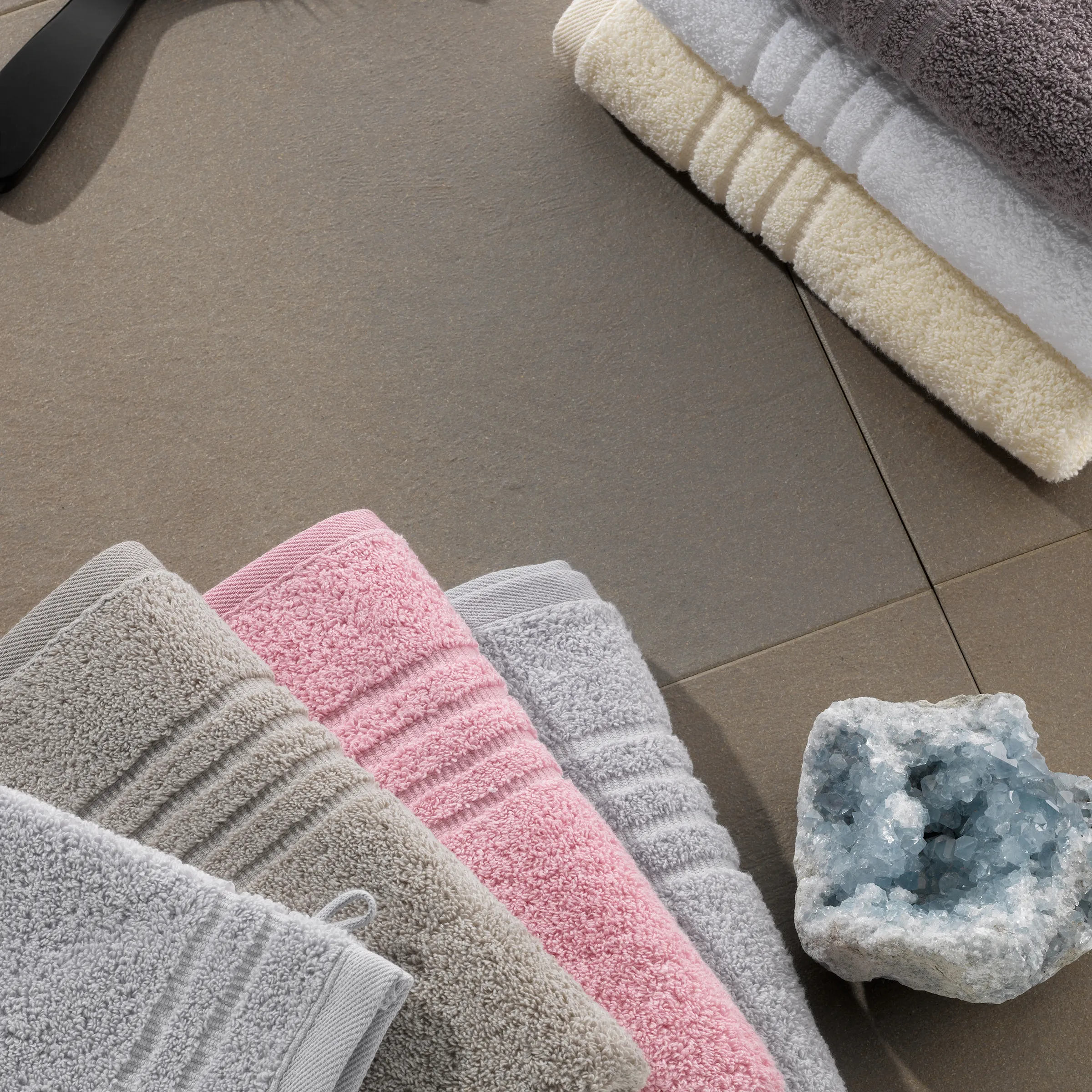 Hochwertige Badtextilien Handtücher in modernen Farben Badezimmer Deko Handtücher in Rosa, Grau und Beige ordentlich auf Badezimmerfliesen arrangiert mit dekorativer Kristallgeode