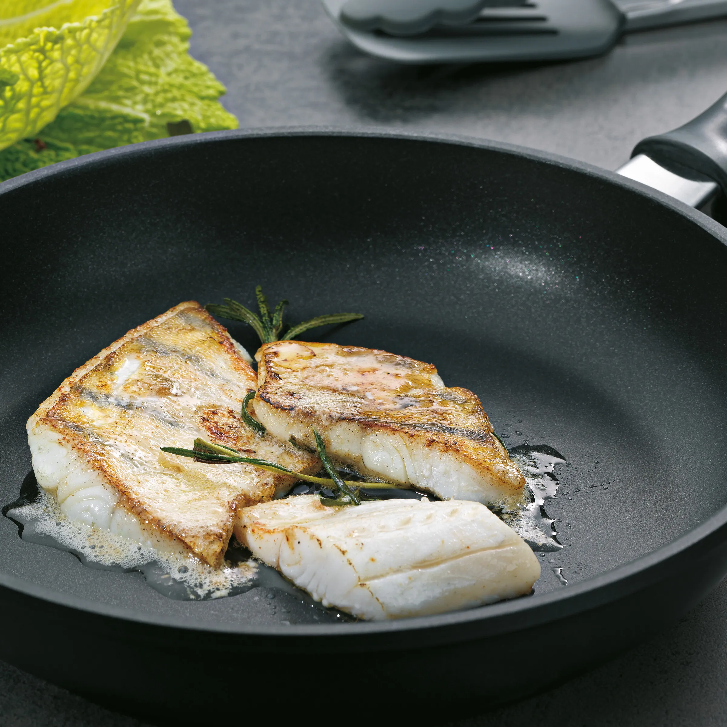 Gebratene Fischfilets in Pfanne - Fisch braten mit Rosmarin Gebratene Fischfilets mit Rosmarin in schwarzer Pfanne auf grauer Arbeitsplatte