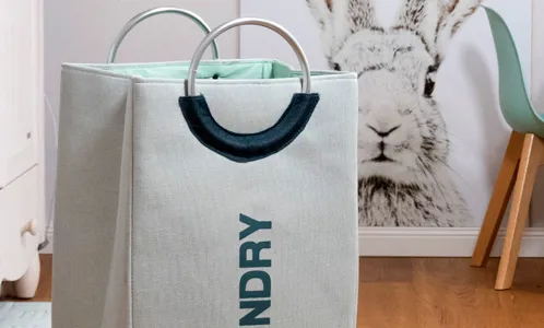 Wäschekorb mit Griffen - Moderne Wäschebox Weiße Wäschekorb mit schwarzem Griff und "LAUNDRY"-Schriftzug in modernem Wohnzimmer neben Kaminholz und Tierposter