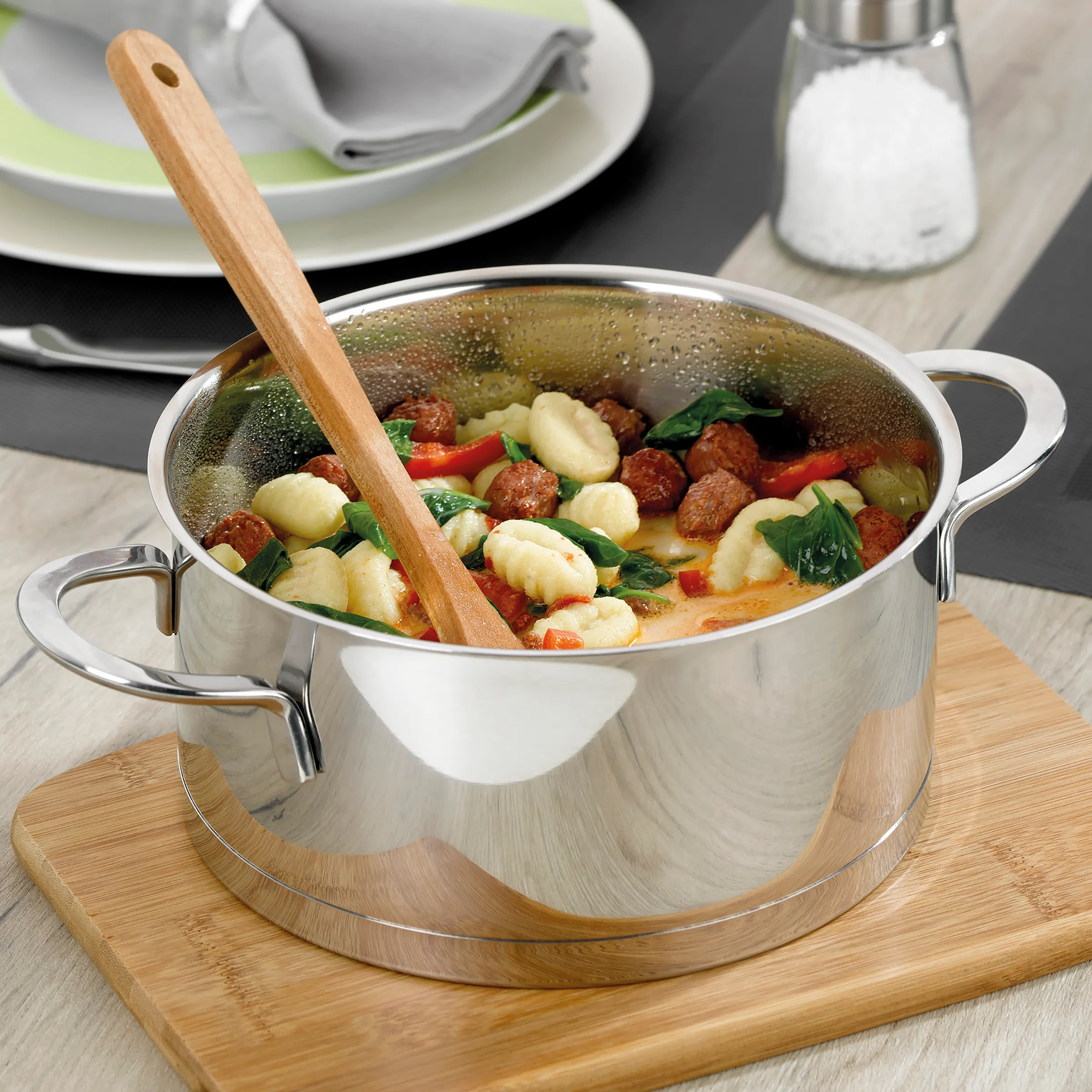 Gnocchi Rezept - Italienischer Eintopf mit frischen Zutaten Weißer Kochtopf mit Gnocchi, Tomaten und Spinat auf Holzbrett mit Holzlöffel