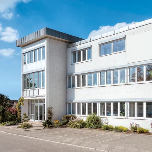 Modernes Bürogebäude Architektur mit Glasfassade Modernes weißes Bürogebäude mit Glasfenstern, grauer Betonumrandung und begrüntem Vorplatz unter blauem Himmel