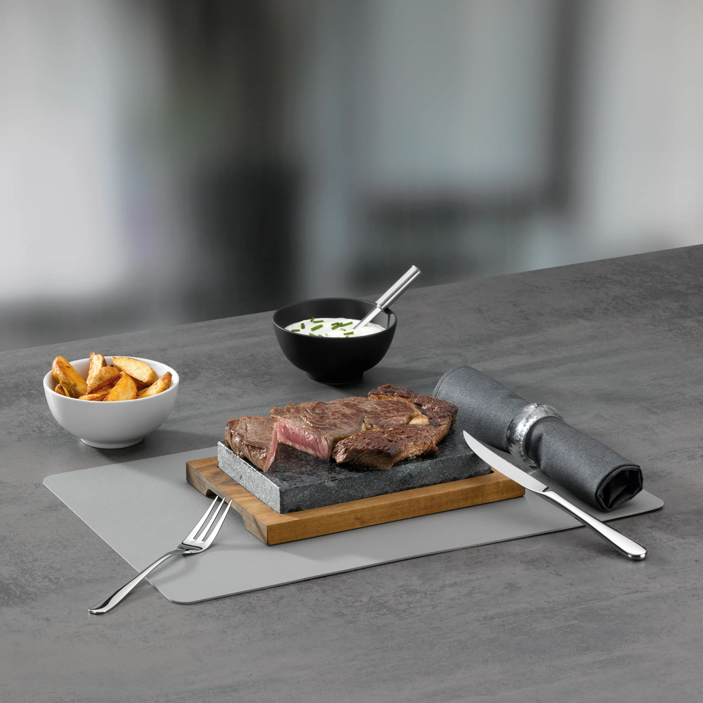 Gegrilltes Steak mit Pommes und Dip - Premium Steakhouse Gericht Gegrilltes Steak auf schwarzem Stein mit goldenen Pommes, Dip und Besteck auf grauem Tisch