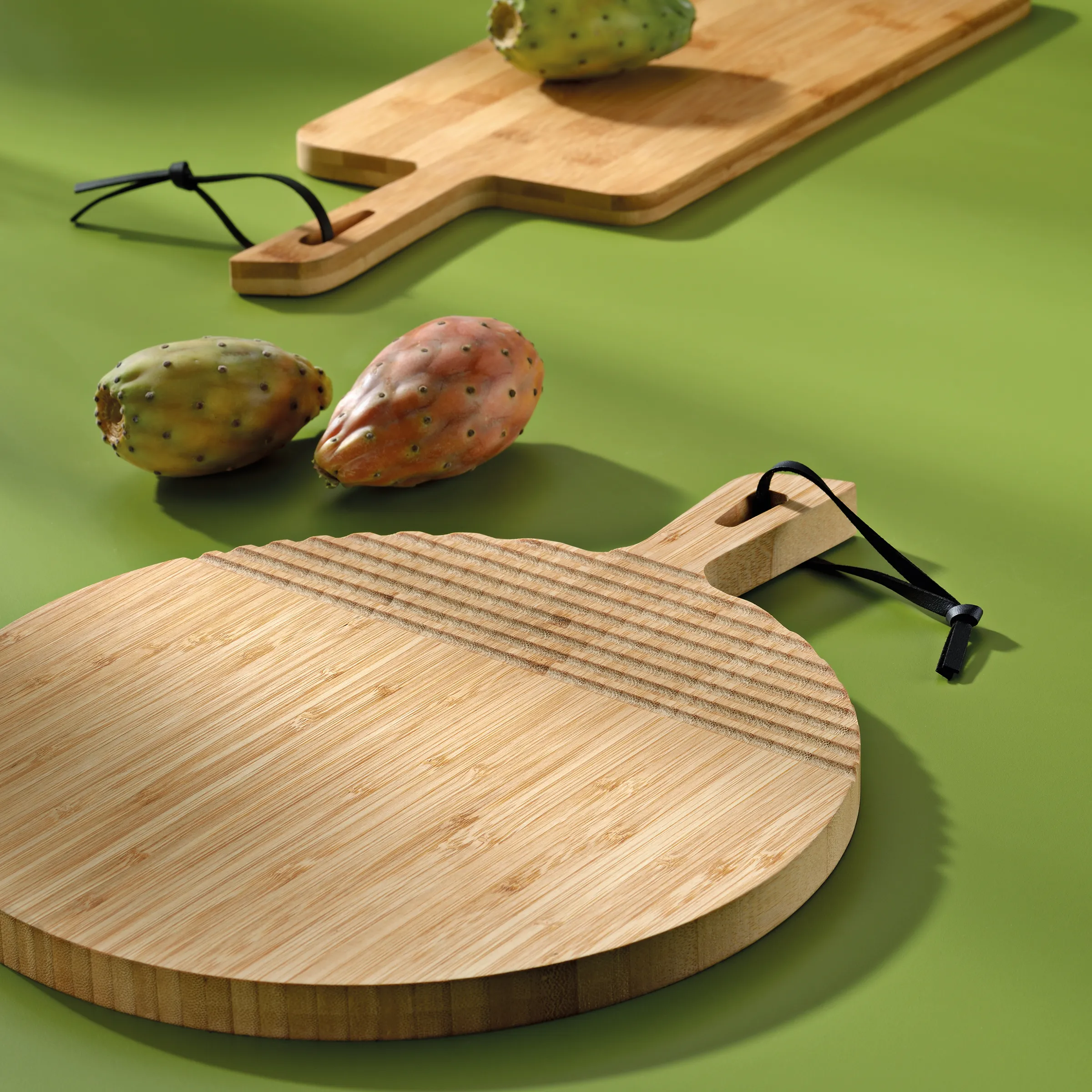 Bambusschneidebretter mit Griffen - Küchenzubehör aus nachhaltiger Holz Runde und rechteckige Bambusschneidebretter mit Kaktusfeigen auf grünem Hintergrund