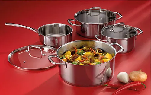 Edelstahl Kochgeschirr Set - Professionelle Töpfe und Pfannen Edelstahl-Kochgeschirr-Set mit Töpfen, Pfanne und Deckel auf rotem Hintergrund mit Gemüse