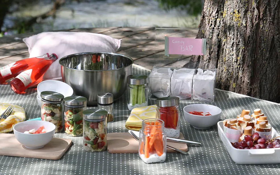 Outdoor Picknick-Buffet mit Candy Bar und Snacks Picknick-Setup im Freien mit Metallkanne, Glasbehältern mit Speisen, Schalen mit Obst und Gebäck, Candy Bar Schild