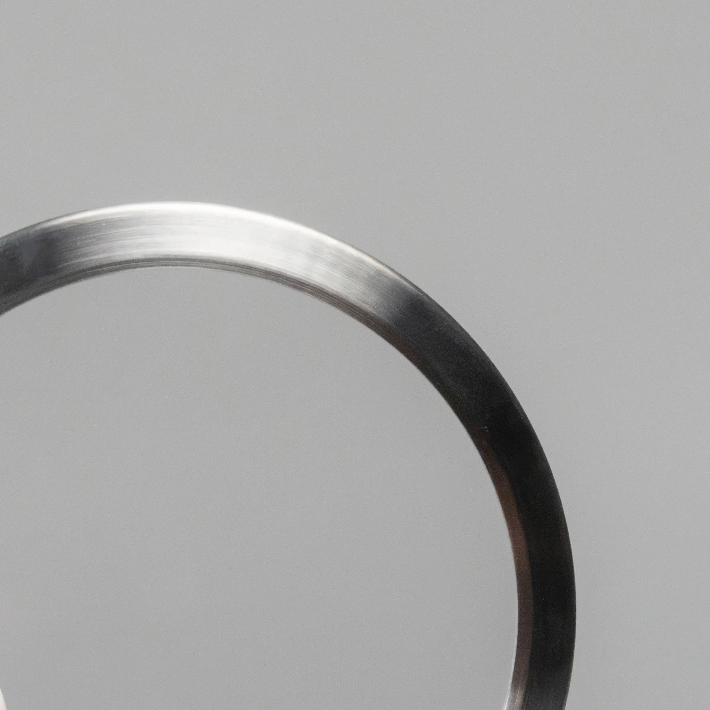 Eleganter Armreif aus Metall mit gebürstetem Finish, Farbverlauf von Silber zu Schwarz auf grauem Hintergrund