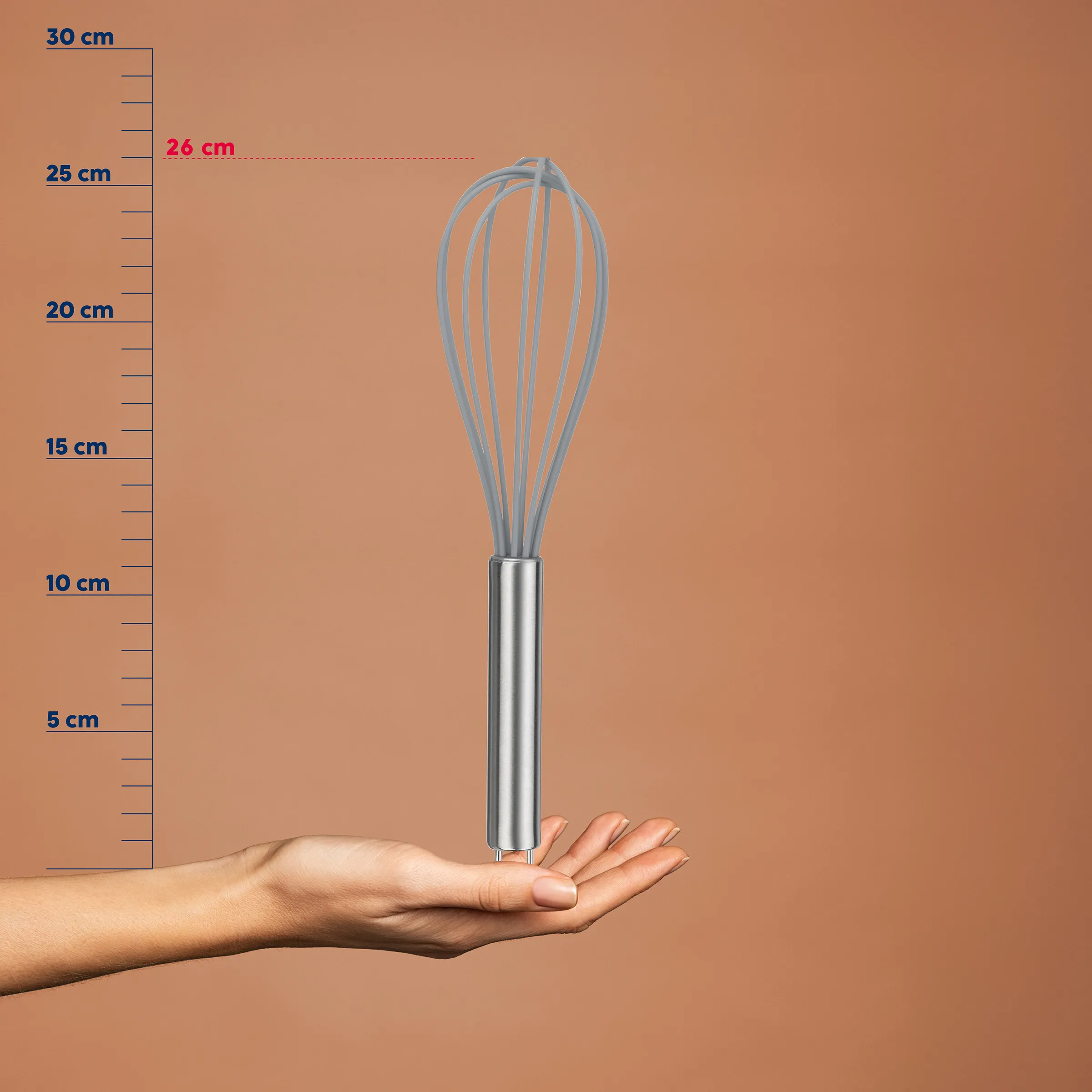 Edelstahl-Schneebesen 26 cm in Hand gehalten vor Maßstab auf braunem Hintergrund