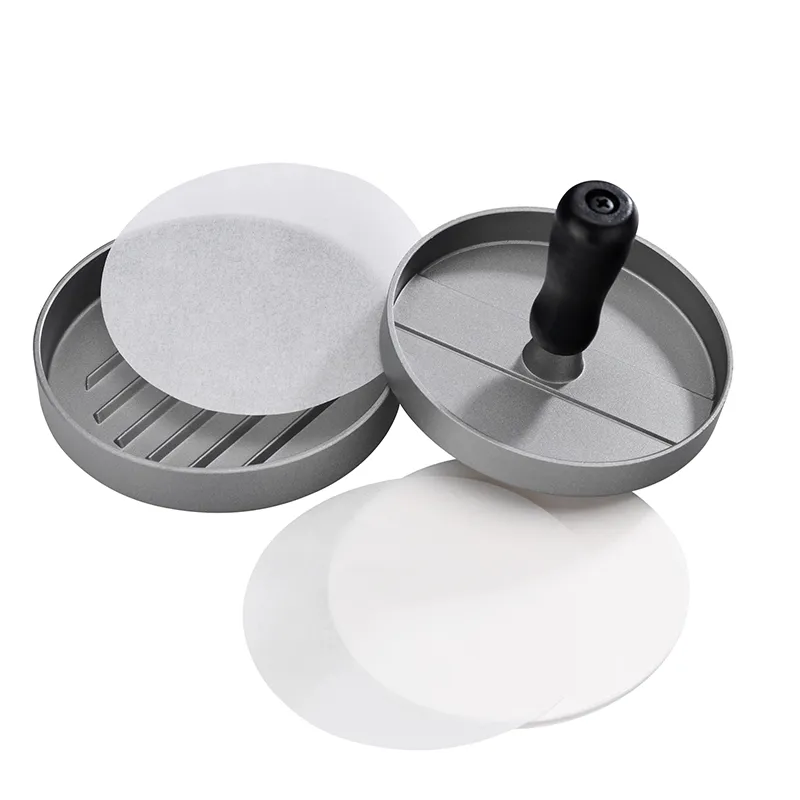 Presse à hamburger en métal avec poignée noire, deux moules à steak et papier antiadhésif sur fond blanc