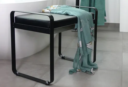 Moderne schwarze Sitzbank mit schwarzem Kunstlederkissen, auf grauem Betonboden mit türkisem Textil draped