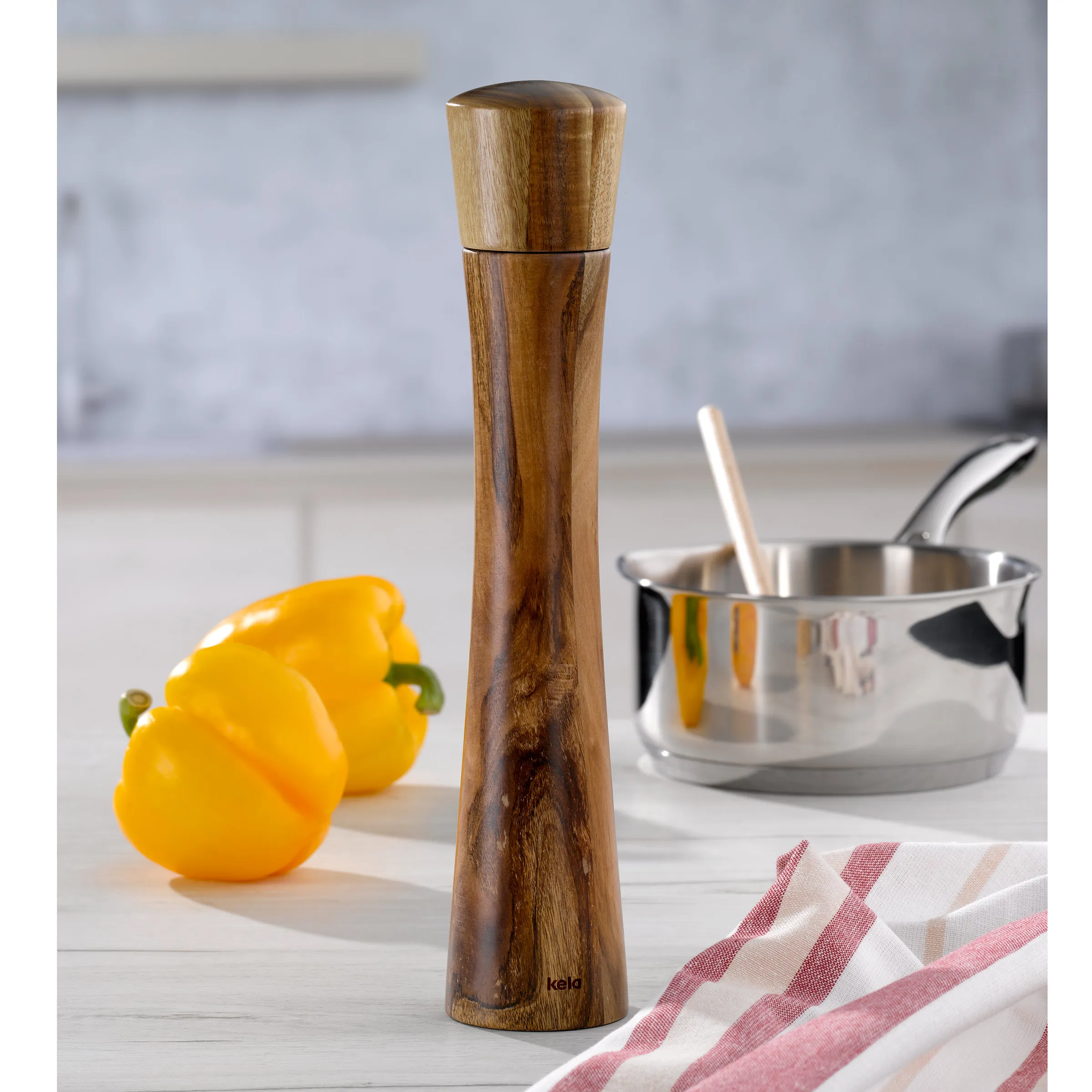 Holzpfeffermühle - Elegante Pfeffer-Gewürzmühle aus Holz Holzpfeffermühle aus Holz mit ovalem Design neben gelben Paprikaschoten und Kochutensilien auf Küchentisch