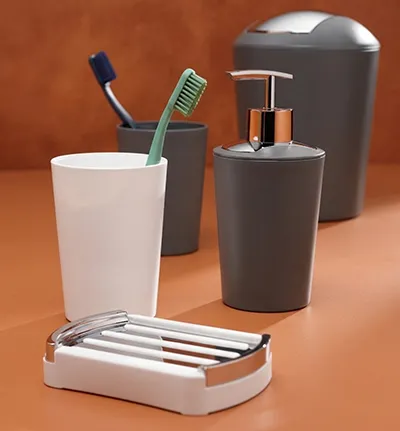 Badezimmer-Set mit weißer Zahnbürstenhalter, weißer Seifenschale, grauem Seifenspender und grauem Mülleimer auf orangefarbenem Hintergrund.