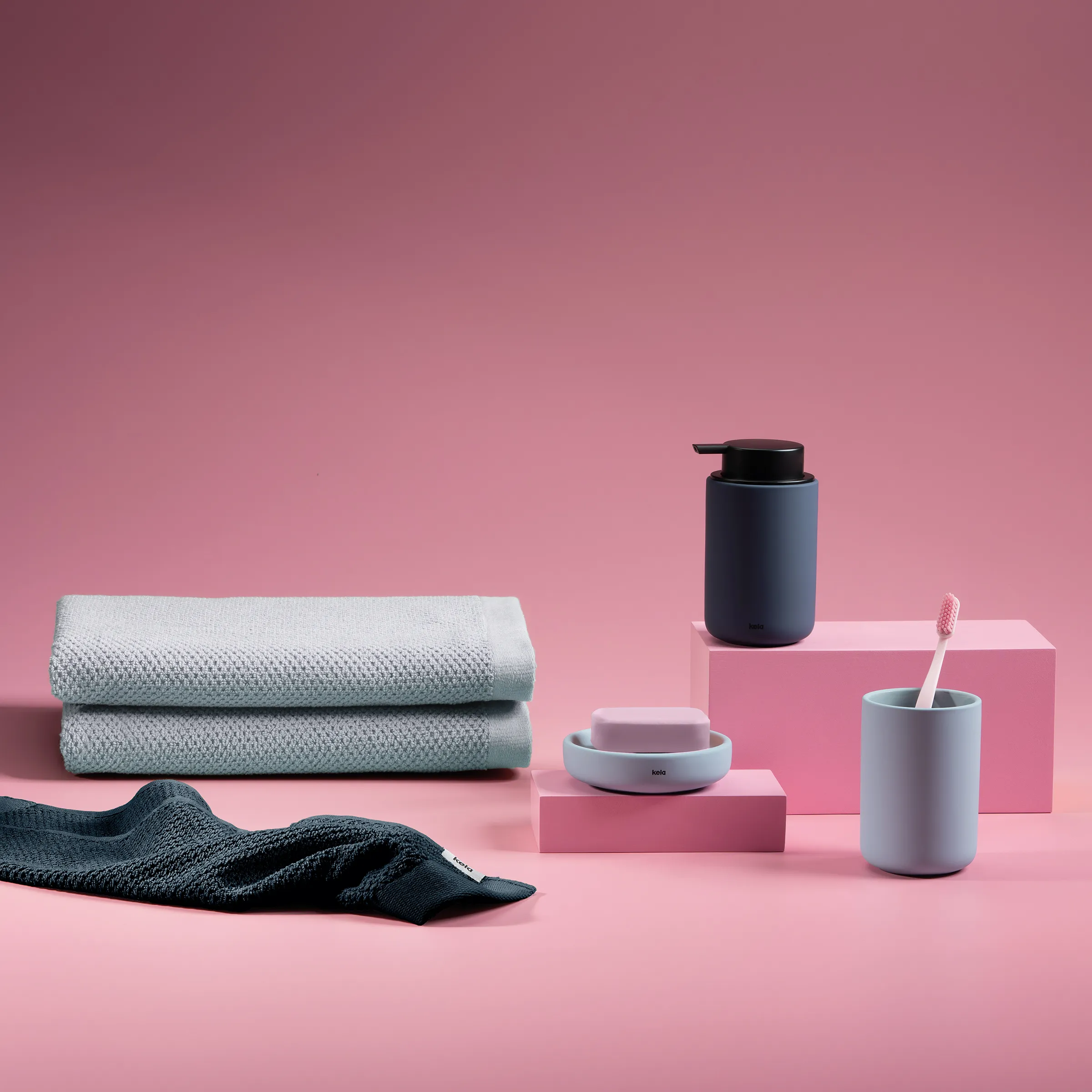 Moderne Badezimmer-Accessoires Set mit Handtüchern und Seifenspender Badezimmer-Accessoires: Handtücher, Seifenspender, Zahnputzbecher und Seifenschale auf rosa Hintergrund