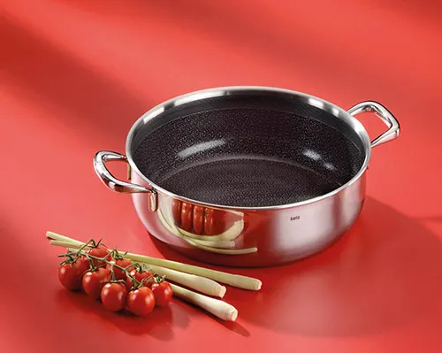 Hochwertiger Kochtopf Antihaftpfanne Edelstahl Küche Edelstahl-Kochtopf mit schwarzer Antihaftbeschichtung auf rotem Hintergrund, daneben Tomaten und Holzspatel