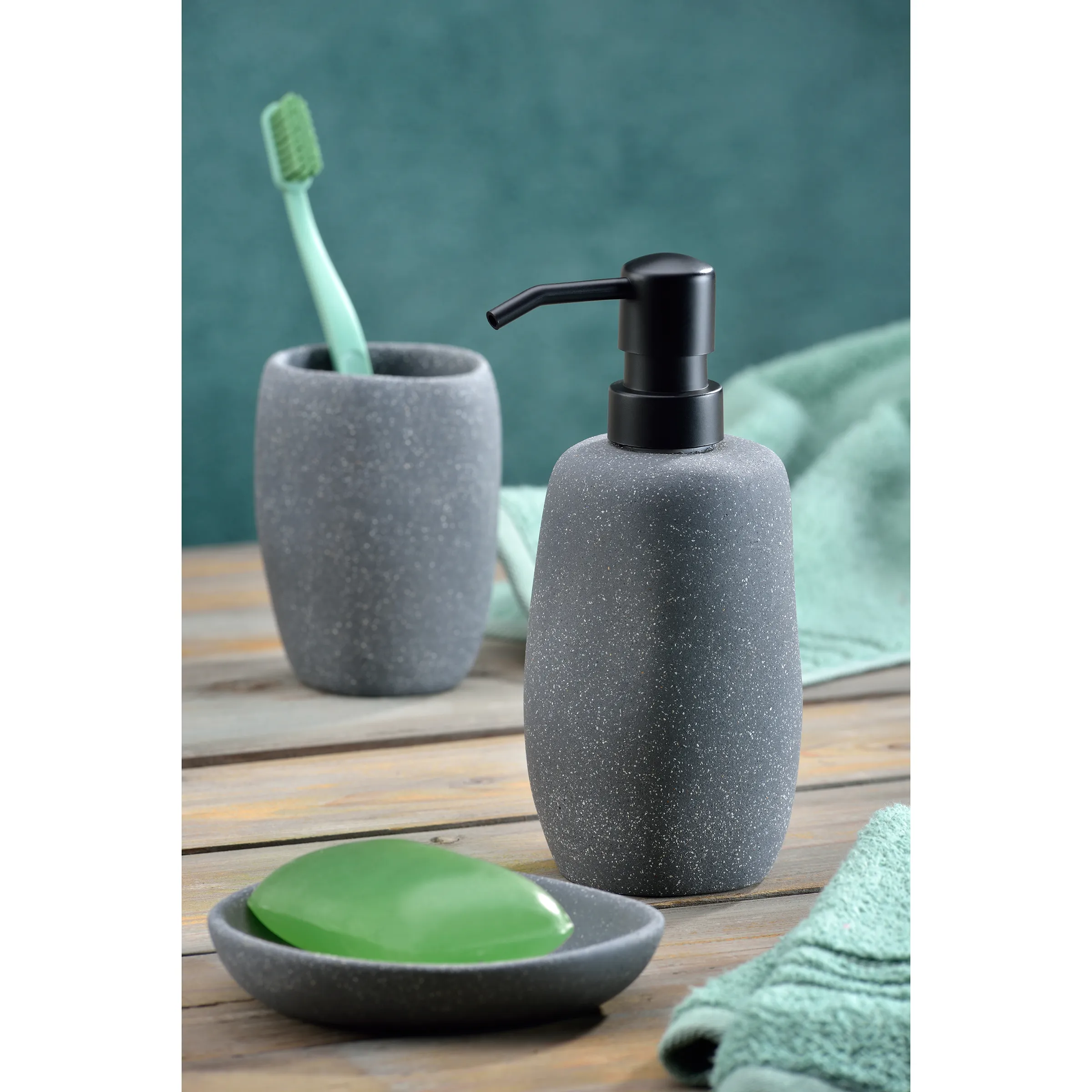 Graues Badezimmer-Set mit Seifenspender, Zahnputzbecher, Seifenschale und mintgrünem Handtuch auf Holz