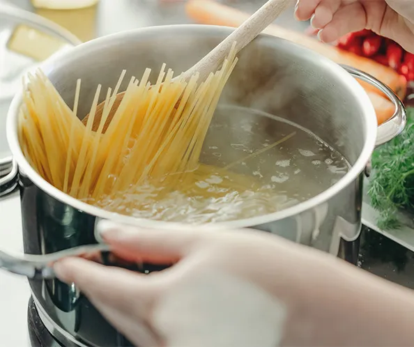 Spaghetti kochen: Pasta in Wasser geben Spaghetti werden mit einer Gabel in kochendes Wasser in einem Topf gegeben
