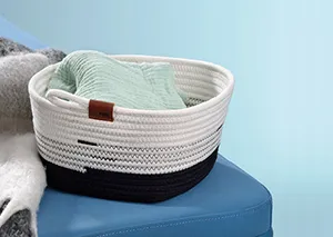 Weiße Aufbewahrungsbox aus Baumwollseil mit schwarzem Baumwollstoff-Einsatz und braunem Lederetikett, teilweise mit grünem Tuch gefüllt