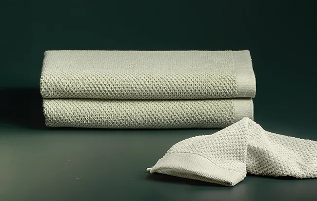 Gestapelte beige Gästehandtücher mit Waffelstruktur auf grünem Hintergrund, zwei ausgebreitete Tücher im Vordergrund