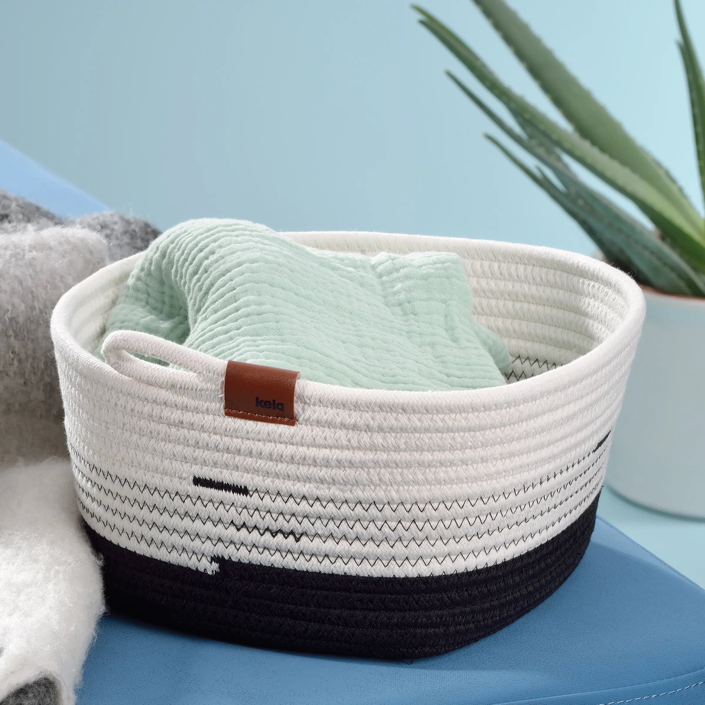 Aufbewahrungskorb aus Baumwollseil mit Ledergriffen - Badezimmer Organizer Weiß-schwarzer Baumwollseilkorb mit Ledergriffen gefüllt mit mintgrünem Handtuch und Aloe-Pflanze im Hintergrund