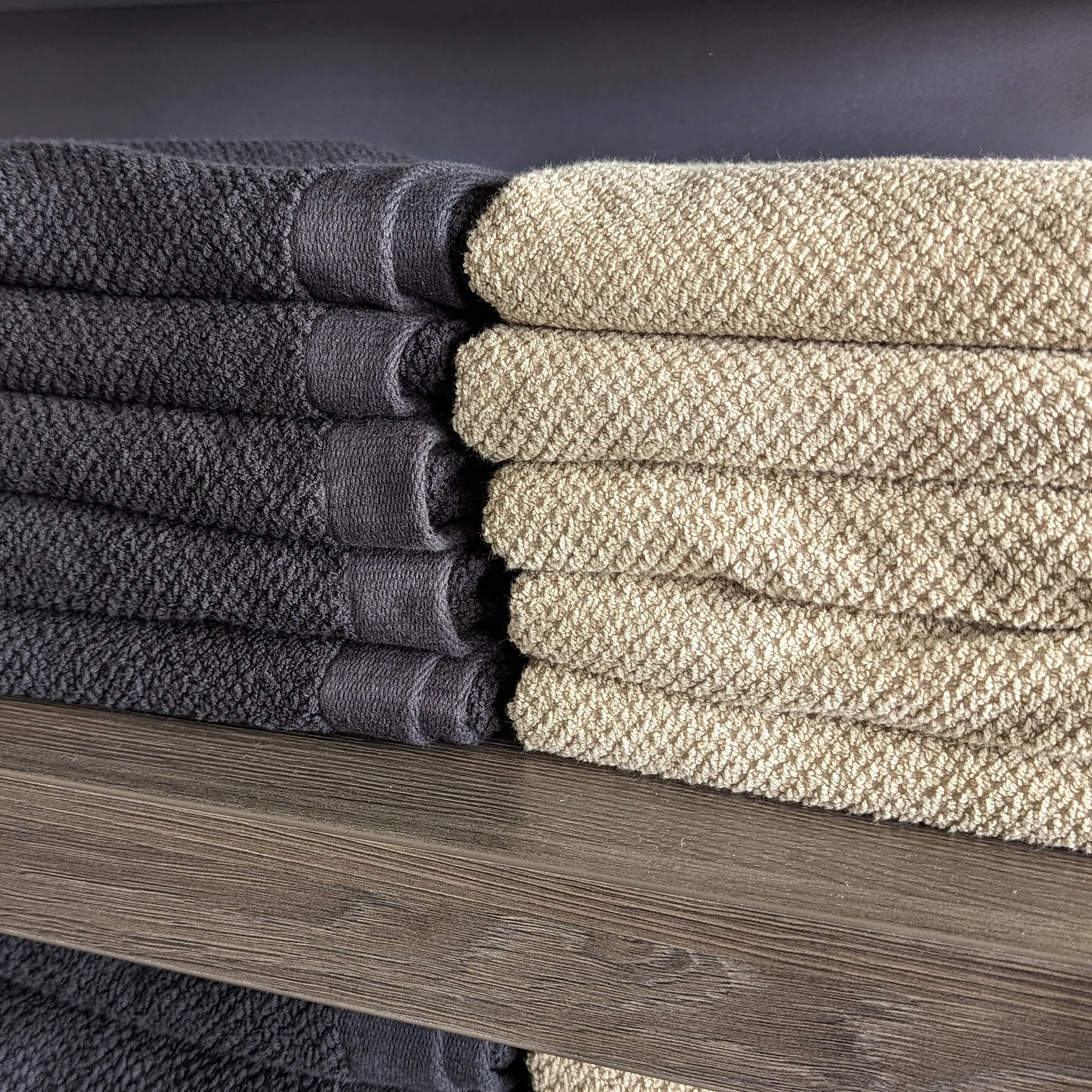 Zwei Stapel Handtücher in Anthrazit und Beige auf Holzregal, ordentlich gefaltet und übereinander geschichtet