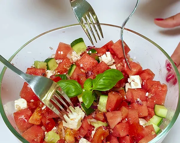 Wassermelonensalat mit Feta und Gurken - Frischer Sommersalat Frischer Wassermelonensalat mit Gurken, Feta-Käse und Basilikum in Glasschüssel mit zwei Gabeln